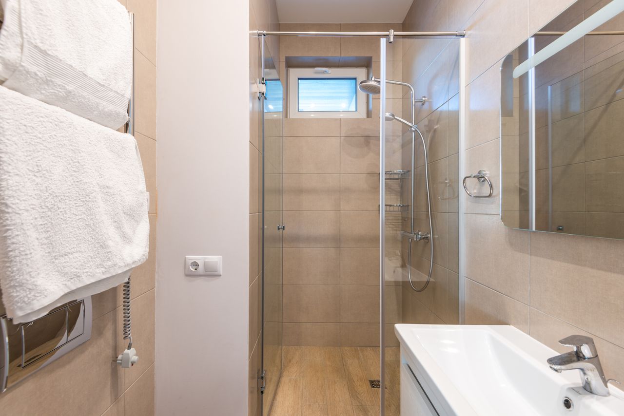 Contemporary bathroom featuring a glass shower, beige tiles, and a sleek sink area.